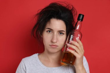 Kırmızı arka planda akşamdan kalma viski şişesi olan bir kadın.