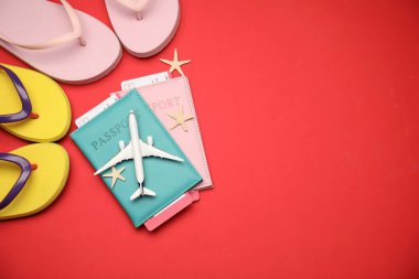Uçak modeli, pasaportlar, uçuş biletleri, parmak arası terlikler ve kırmızı arka planda yıldız balıkları. Metin için boşluk