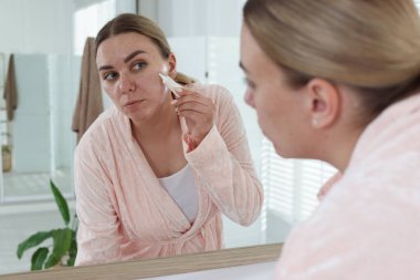 Kadın evin içinde aynanın yanında yüzüne krem sürüyor. Sivilce tedavisi