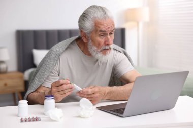 Termometresi olan kıdemli bir adam içeride bilgisayarla doktorla görüşüyor.