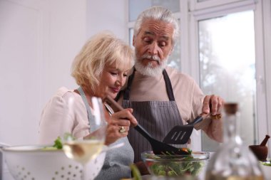 Spatulası olan yaşlı bir çift mutfakta birlikte yemek pişiriyor.
