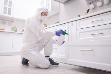 Koruyucu kıyafetli haşereci evde böcek ilacı sıkıyor, düşük açılı.