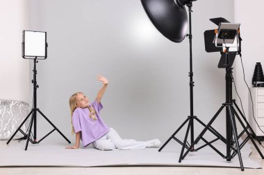 Açık gri arka plandaki küçük kız profesyonel ekipmanlarla fotoğraf stüdyosunda.