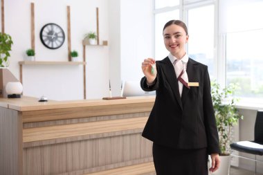 Üniformalı gülen resepsiyonist otelin misafir odasının anahtarını veriyor.