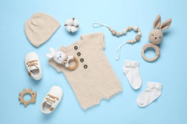 Açık mavi arka planda şirin bebek kıyafetleri ve aksesuarlar, düz yatış.