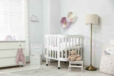 Şık beyaz beşik, çekmeceler, lamba, oyuncaklar ve dekorasyon malzemeleri bebek odasında. İç tasarım