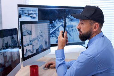 Güvenlik görevlisi güvenlik kameralarını izliyor ve ofiste telsiz kullanıyor.