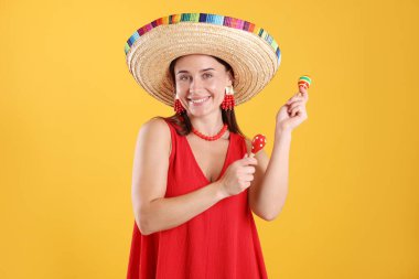 Sarı arka planda marakas çalan şapkalı mutlu kadın.