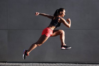 Spor kıyafetli bir kadın binanın yanında koşuyor.