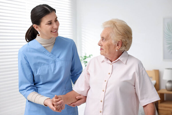 Nurse assisting senior woman indoors. Home health care service