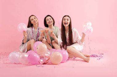 Pijama partisi. Pembe arka planda parıldayan balonları olan mutlu arkadaşlar.
