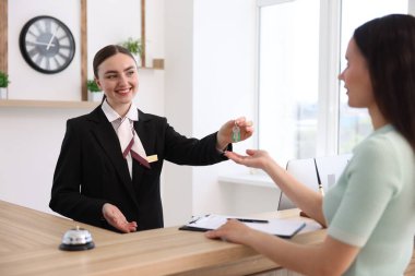 Üniformalı gülen resepsiyonist otel resepsiyonundaki müşteriye misafir odasının anahtarını veriyor.