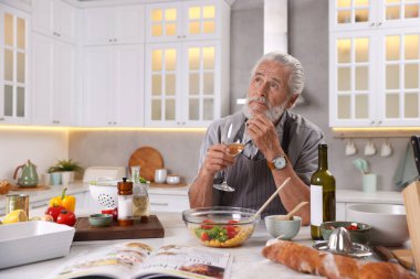 Düşünceli yaşlı adam mutfakta yemek yaptıktan sonra beyaz şarap içiyor.