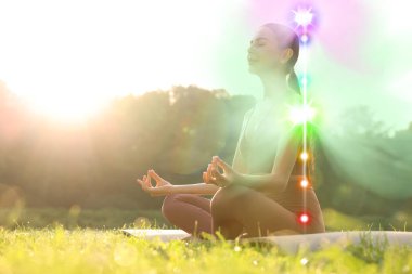 Lotus 'ta meditasyon yapan kadın güneşli bir sabahta doğada poz veriyor. Yedi çakra parlıyor