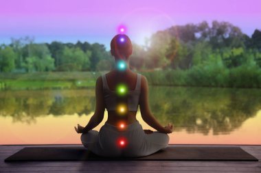 Lotus 'ta meditasyon yapan kadın doğada, arka planda poz veriyor. Yedi çakra parlıyor