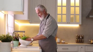 Mutfakta lavabonun üstünde taze marul yıkayan yaşlı bir adam, kamera hareket ediyor.