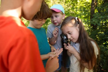 Çocuklar doğadaki büyüteçle salyangoza bakıyor.