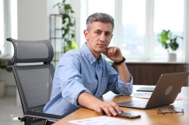 Ofiste dizüstü bilgisayar ve akıllı telefonla çalışan bir iş adamı.