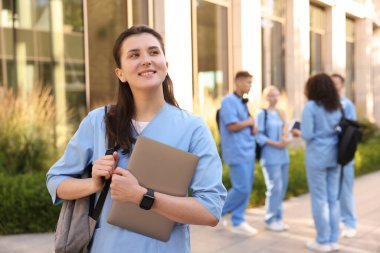 Açık hava binasının yakınında sırt çantası ve dizüstü bilgisayarı olan mutlu tıp öğrencisi, seçici odaklı.