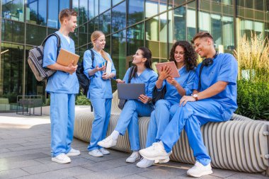 Üniformalı bir grup tıp öğrencisi açık hava binasının yakınında birlikte okuyorlar.