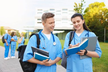 Sırt çantalı ve defterli tıp öğrencileri açık havada, seçici bir odak noktası.