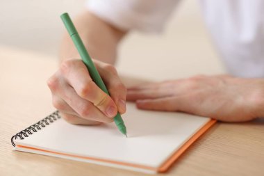 Ahşap masadaki kalemle arka planı bulanıklaştıran, yakın plan, not defterine yazan adam