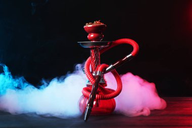 Siyah arka planda sigara dumanı olan ahşap masada nargile.