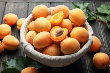 Sepette taze kayısılar ve ahşap masada yeşil yapraklar, yakın plan.