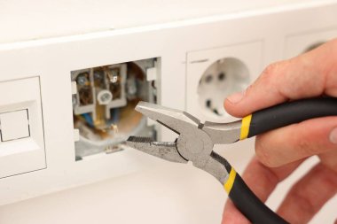 Kapalı mekanda penseyle prizleri tamir eden adam, yakın plan.