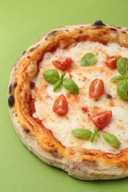 Domatesli lezzetli pizza ve yeşil masada fesleğen, yakın plan.