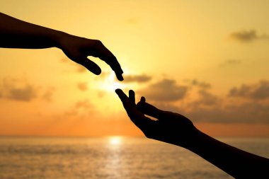 Kadın ve erkek gün batımında deniz manzarasına karşı ellerini birbirine uzatıyor.