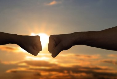 Erkek ve kadın gün batımında gökyüzüne yumruk tokuşturuyor, ellerinin yakınına.