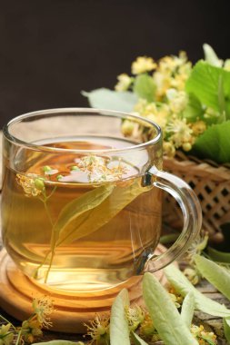 Fincanda lezzetli ıhlamur çayı, ahşap masada yapraklar ve çiçekler koyu arka planda, yakın plan.