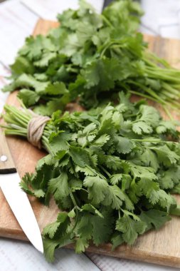 Tahta kesme tahtası taze kişniş ve bıçak beyaz ahşap masada, yakın plan.