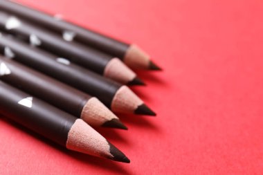 Kırmızı arka planda birçok kaş kalemi var, yakın plan. Metin için boşluk