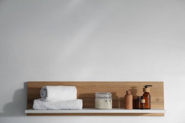 Beyaz zemin üzerinde kozmetik ürünler ve havlular olan ahşap bir raf. Metin için boşluk