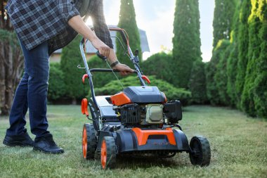 Bahçedeki çim biçme makinesinin marş kablosunu çeken adam, yakın plan.