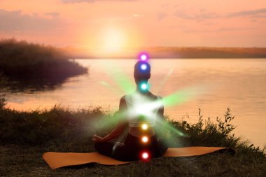 Lotus 'ta meditasyon yapan kadın gün doğumunda nehrin kenarında poz veriyor. Yedi çakra parlıyor