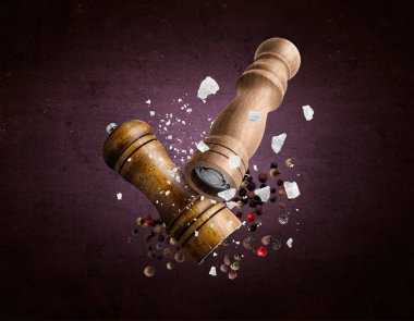 Tuz ve biber değirmenleri, koyu mor arka planda uçuşan kaba tuz ve biber taneleri.