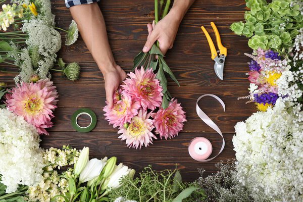 Профессиональный флорист делает букет цветов за деревянным столом, вид сверху