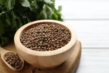 Kişniş tohumu ve taze kişniş beyaz ahşap masada, yakın plan.