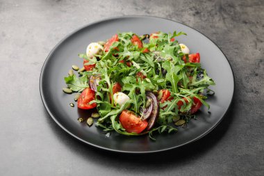 Lezzetli salata roka, mozzarella ve sebzeler gri masada, yakın plan.