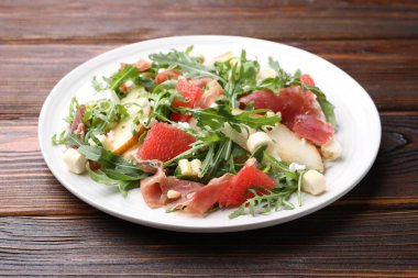 Lezzetli salata roka, prosciutto, peynir, armut, greyfurt ve ahşap masada fındık, yakın plan.