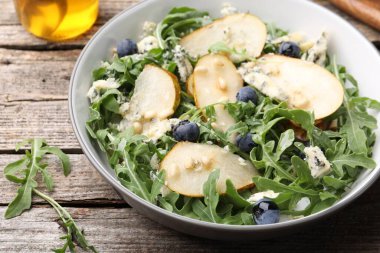 Lezzetli salata roka, armut, mavi peynir, fıstık ve yabanmersinleri ahşap masada, yakın plan.