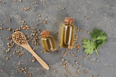 Şişelerde Aromatik yağ, kişniş yaprakları ve kişniş tohumları gri masada, düz yatıyordu.