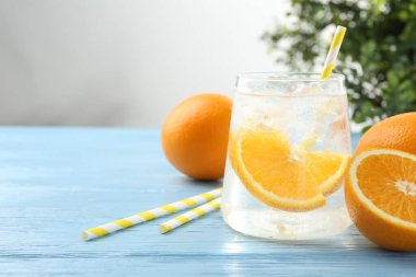 Bardakta portakal dilimleri, açık mavi ahşap masada taze meyveler ve pipetler olan köpüklü su, yakın plan. Metin için boşluk