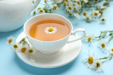 Lezzetli papatya çayı ve açık mavi arka planda çiçekler, yakın plan.