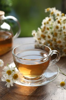 Cam bardakta romatik çay ve ahşap masada papatya çiçekleri, yakın plan.