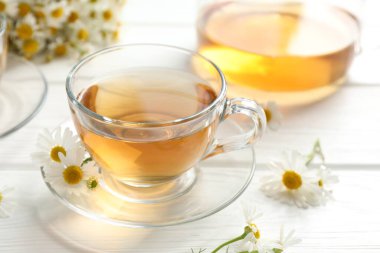 Cam fincanlarda romatik çay ve beyaz ahşap masada papatya çiçekleri, yakın plan.