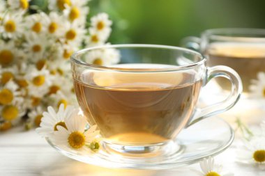 Cam fincanlarda romatik çay ve beyaz ahşap masada papatya çiçekleri, yakın plan.